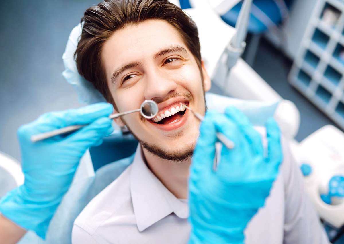 A smiling man having his teeth examined with a dental mirror